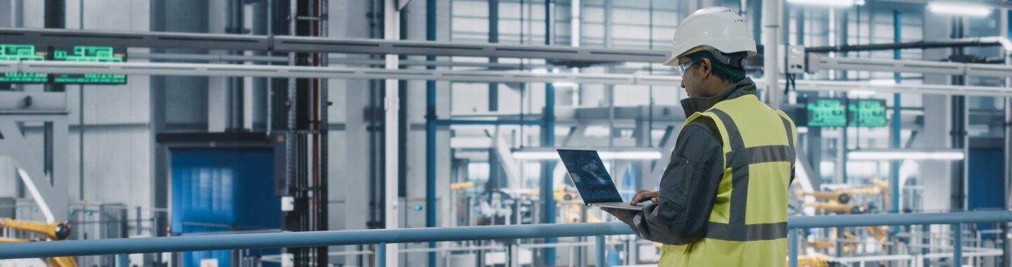 a man using a laptop in a factory.