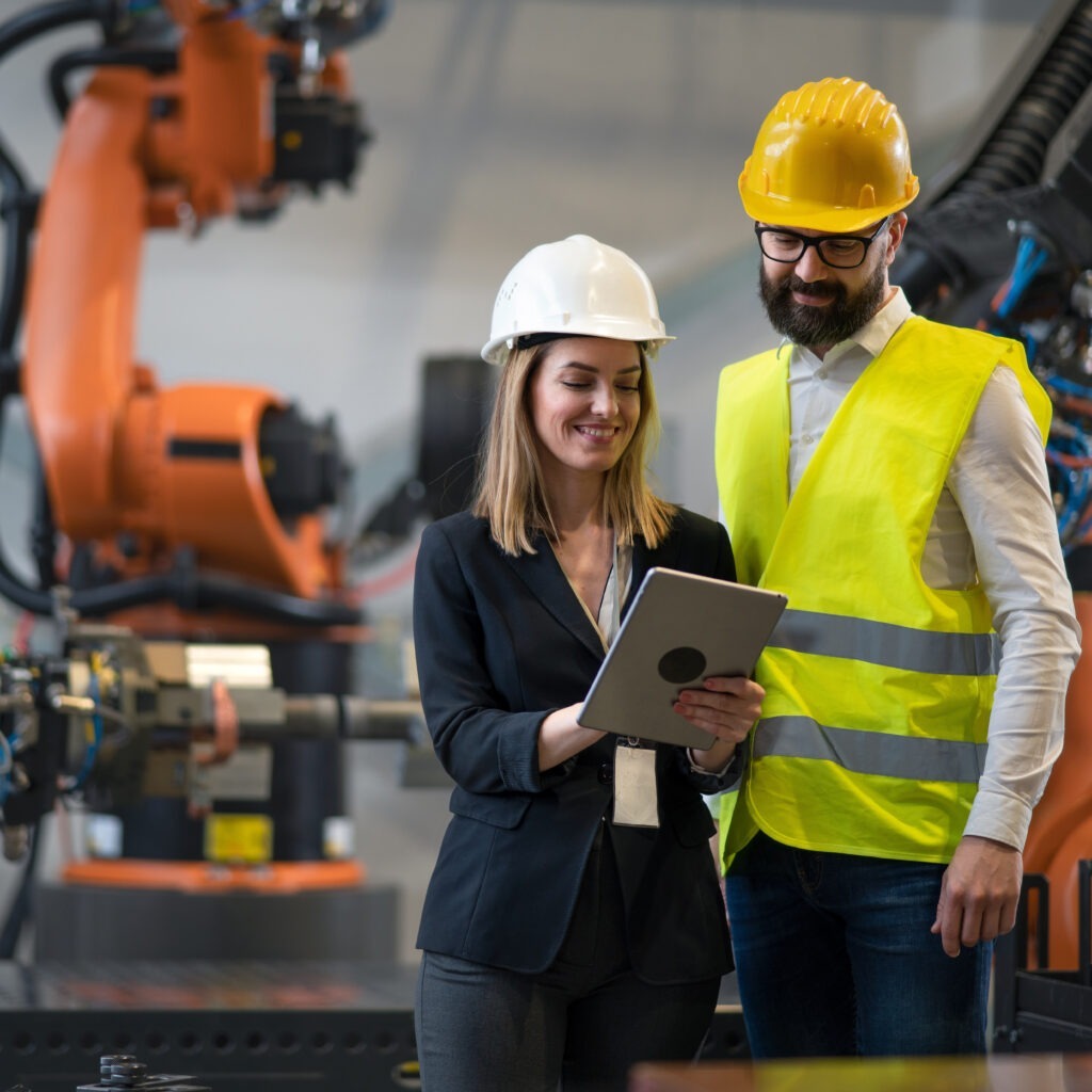 Chief engineer and project manager in modern industrial factory with robot arms talking and planning optimization of production.